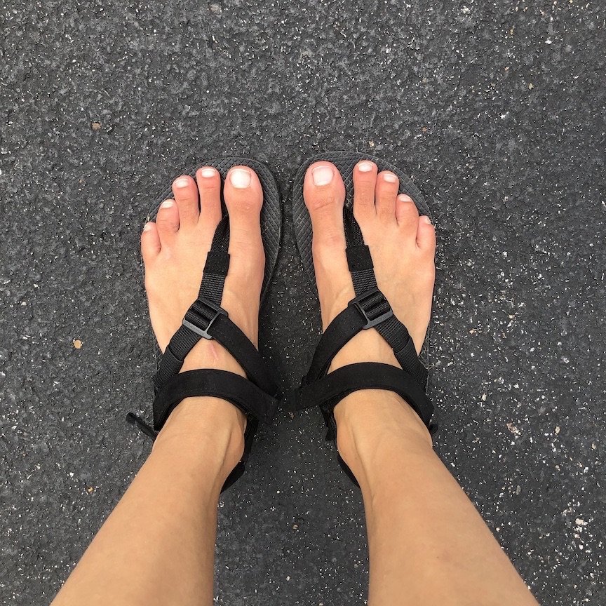 discount code for barefoot shoes at the black Shamma Warrior Sandals shown on feet with the Power Straps on, top down on view on asphalt