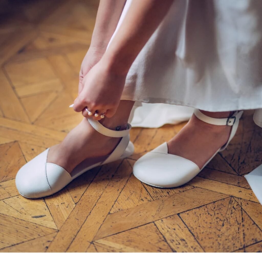 A close up of a bride's feet wearing Ahinsa Shoes barefoot wide toe box ballet flats in white