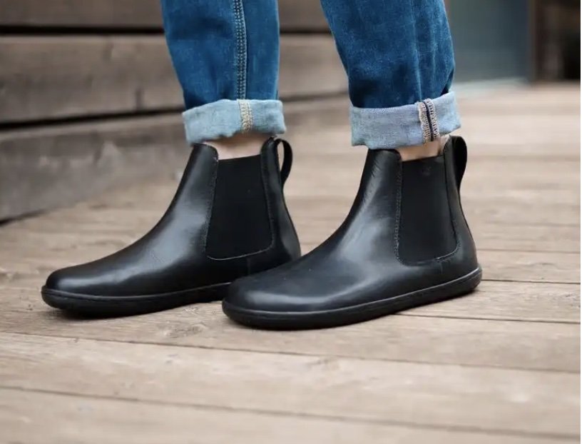 A close up side view of a pair of legs wearing Angles Nyx barefoot chelsea boots in shiny black