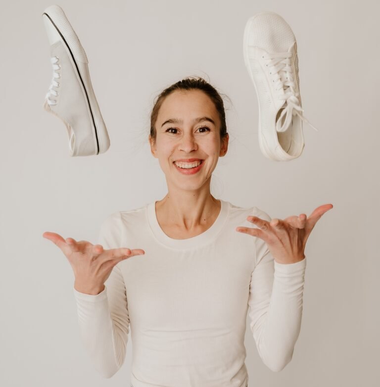 A woman named Anya looking and smiling at the camera throwing two barefoot shoes up in the air