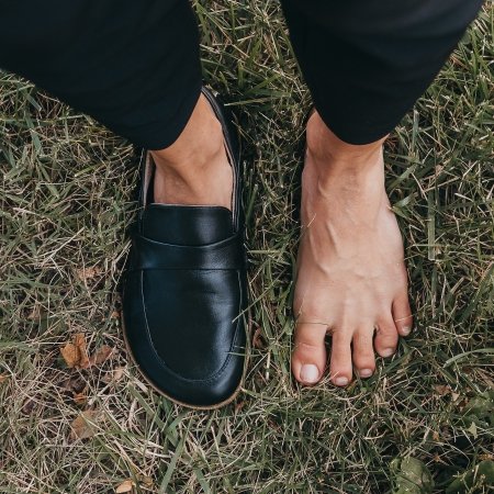 Top down view of one bare foot and one foot wearing a black Dalia Loafer from Anya's Shop with a wide anatomical toe box and flexible outsole