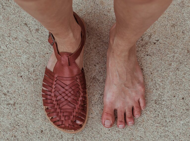 Top down view of a woman with wide feet wearing 1 Origo Huaraches by Anya Sandal in Reddish brown woven leather and one bare foot to show the anatomical toe box