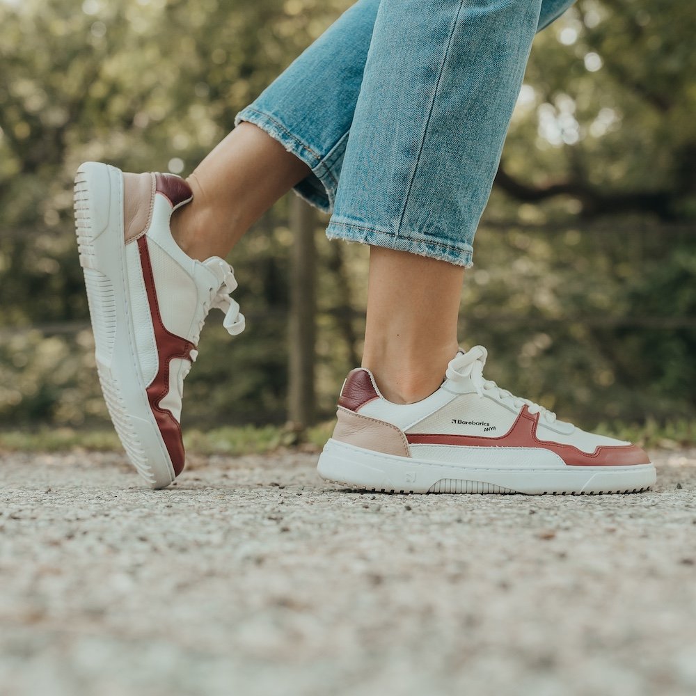 A side view of a pair of legs and feet wearing jeans and custom Barebarics X Anya Zings that are white with burgundy accents