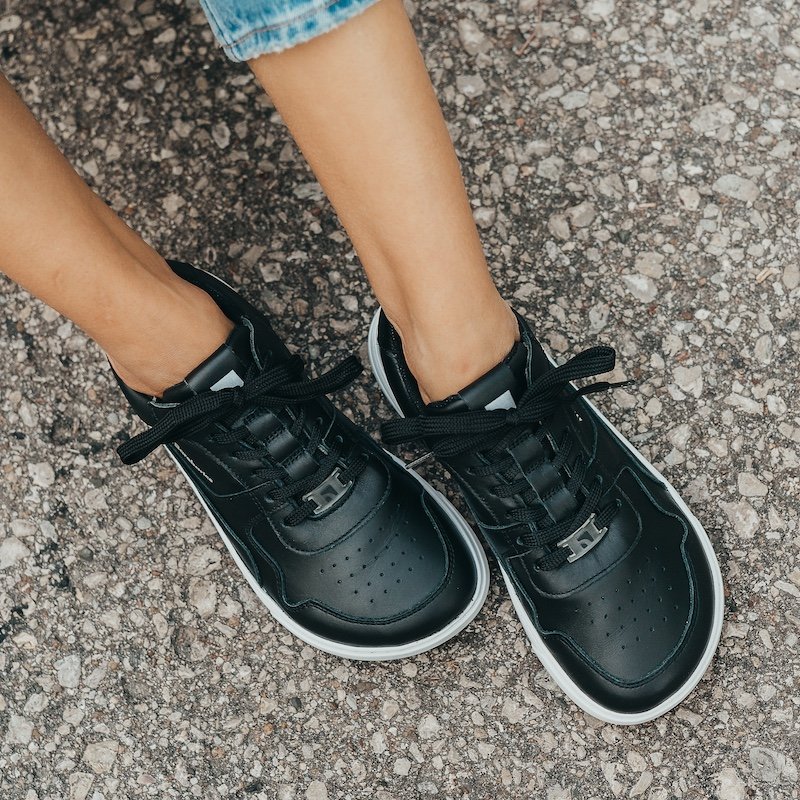 a top down view of a pair of feet wearing Barebarics Zings wide toe box foot shaped barefoot sneakers in black leather