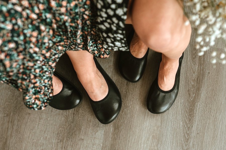 Top down view of two pairs of feet in floral skirts both wearing Groundies Lily barefoot ballet flats, in regular and wide width