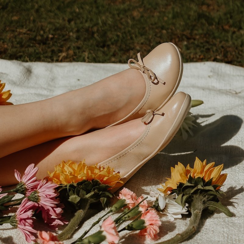 Groundies Ruby barefoot beige flats being worn outside on a picnic blanket surrounded by flowers