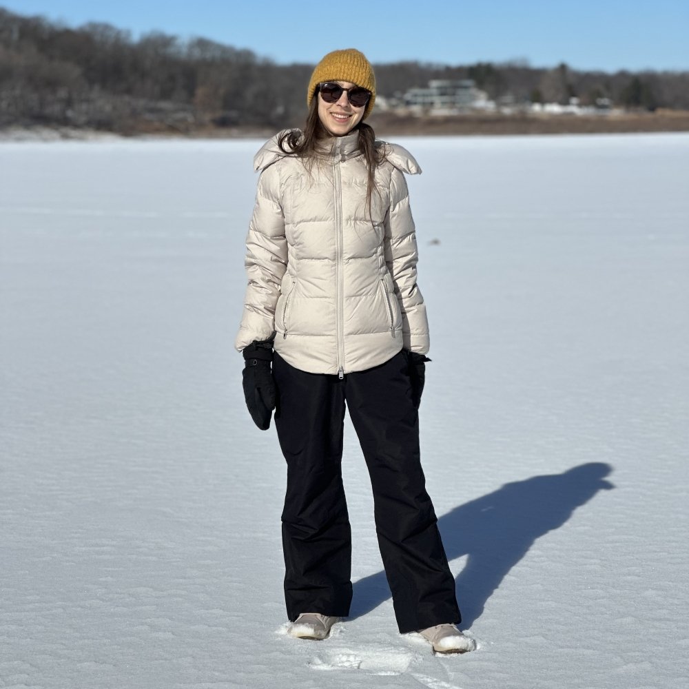 A full body view of a woman standing in the snow decked out in snow gear. She is smiling at the camera. She has a pair of Be Lenka Arctic Edge snow boots on her feet