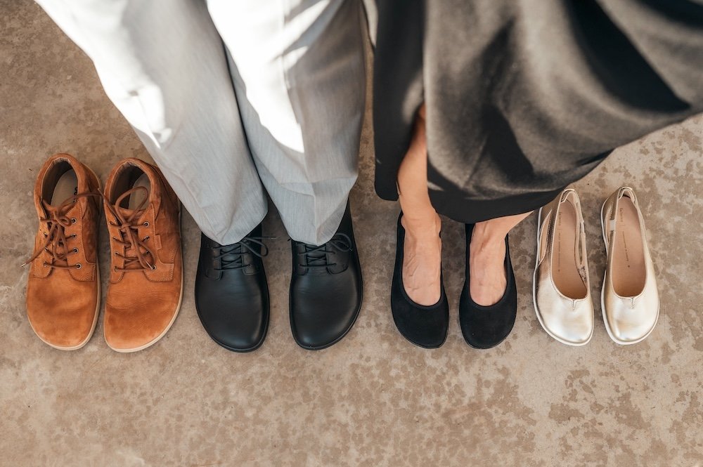 A top down view of the legs and feet of a man and a woman standing side by side, each wearing dressy barefoot dress shoes for men and women by Be Lenka barefoot brand