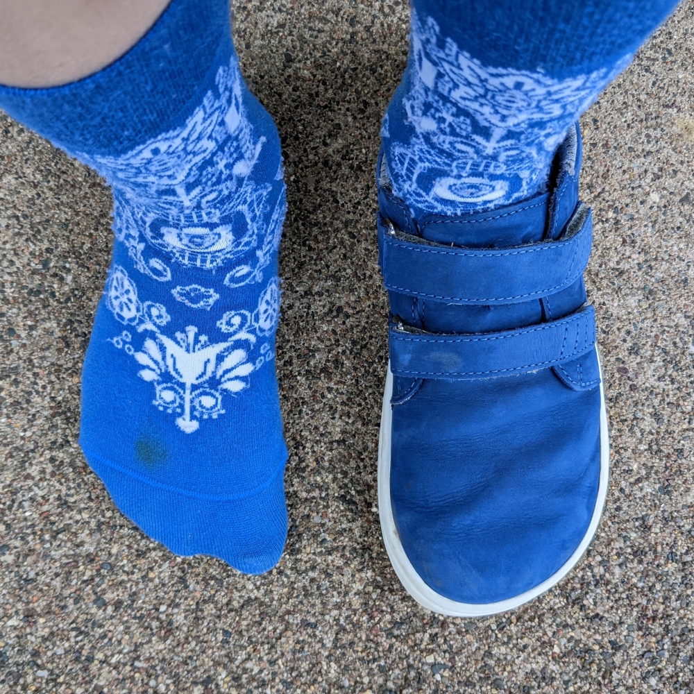 Top down view of one kids foot in Be Lenka Barefoot socks and the other foot in matching blue Be Lenka Jolly sneakers with zero drop outsole and extra wide toe box