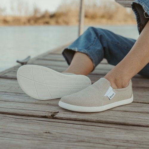 Be Lenka Eazy Neo being worn by a person sitting on a sock. The side of the barefoot sneaker and the sole are focus of the picture. You can see the extra wide toe box shape on the outsole