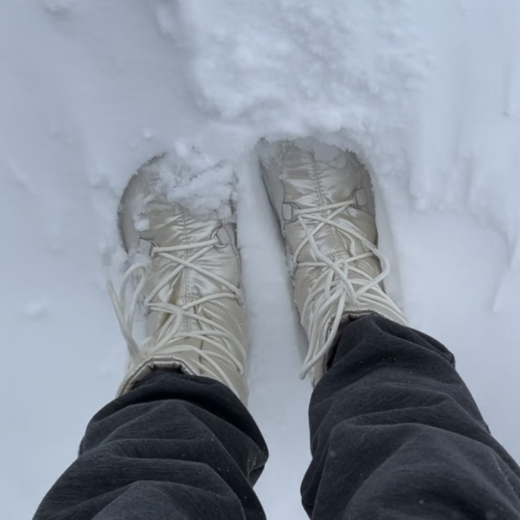 Top down view of a pair of feet standing in moderately deep snow wearing Be Lenka Snowfoxf wide toe box warm winter boots
