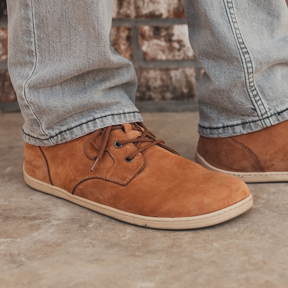 A close up side view of a man's feet standing on concrete wearing grey pants and Be Lenka synergy cognac barefoot dress shoes for men