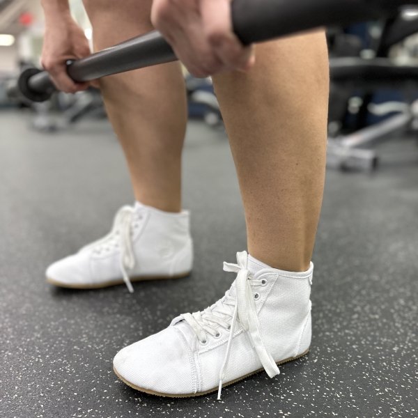 A person lifting weights in Bearfoot Shoes ursus hightop canvas barefoot gym shoes in white.