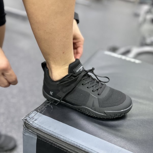 A side view of one Notorious Lift black barefoot gym shoes about to step up on a box. The grippy zero drop outside is keeping the foot steady.