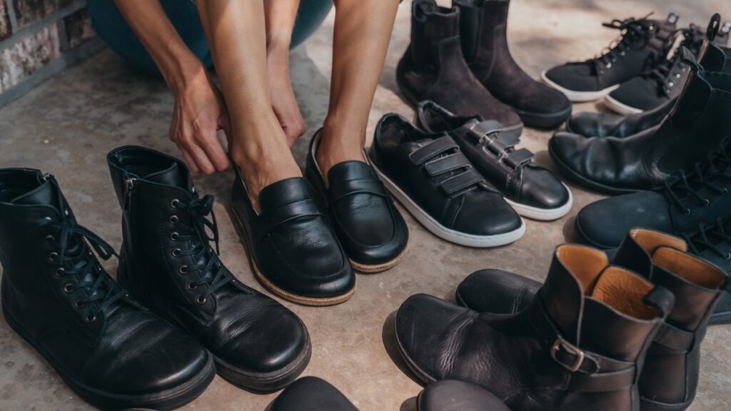 An array of black barefoot shoes loosely arranged around a person putting on a pair of black barefoot loafers.