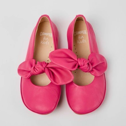 Stock image of pink ballet flats for girls in a bright pink leather with tied strap detail across the foot.