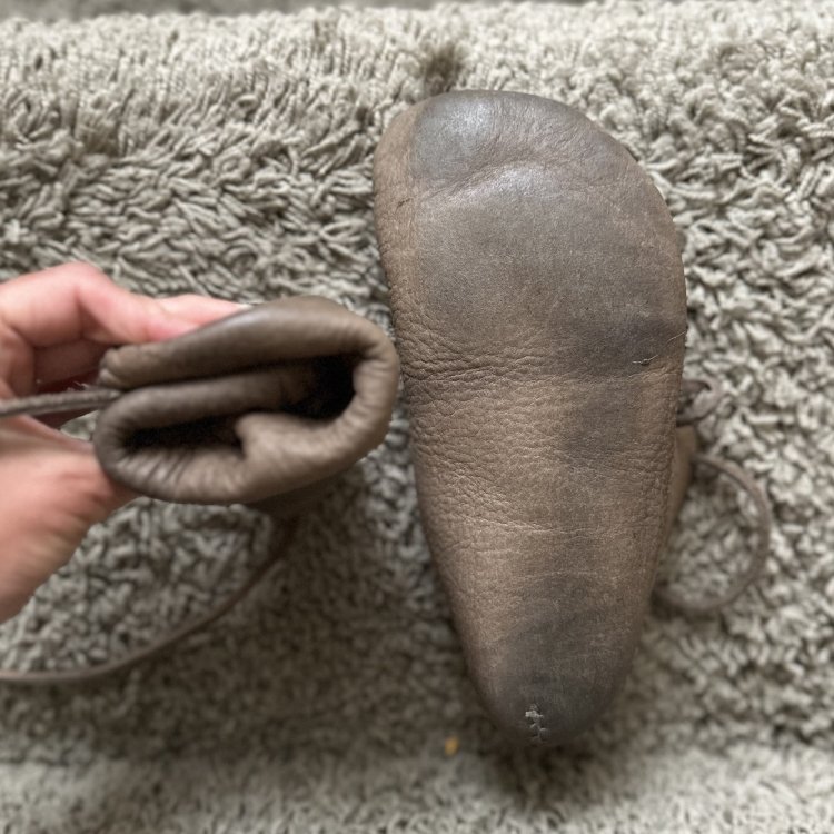 A hand holding 1 Earthing Moccasin into a tight ball to show flexibility and the leather outsole is visible on the other shoe
