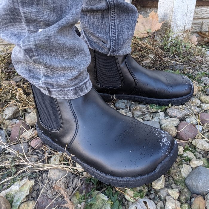 Feelgrounds Kids vegan barefoot chelsea boot being worn with gray skinny jeans on rocky ground