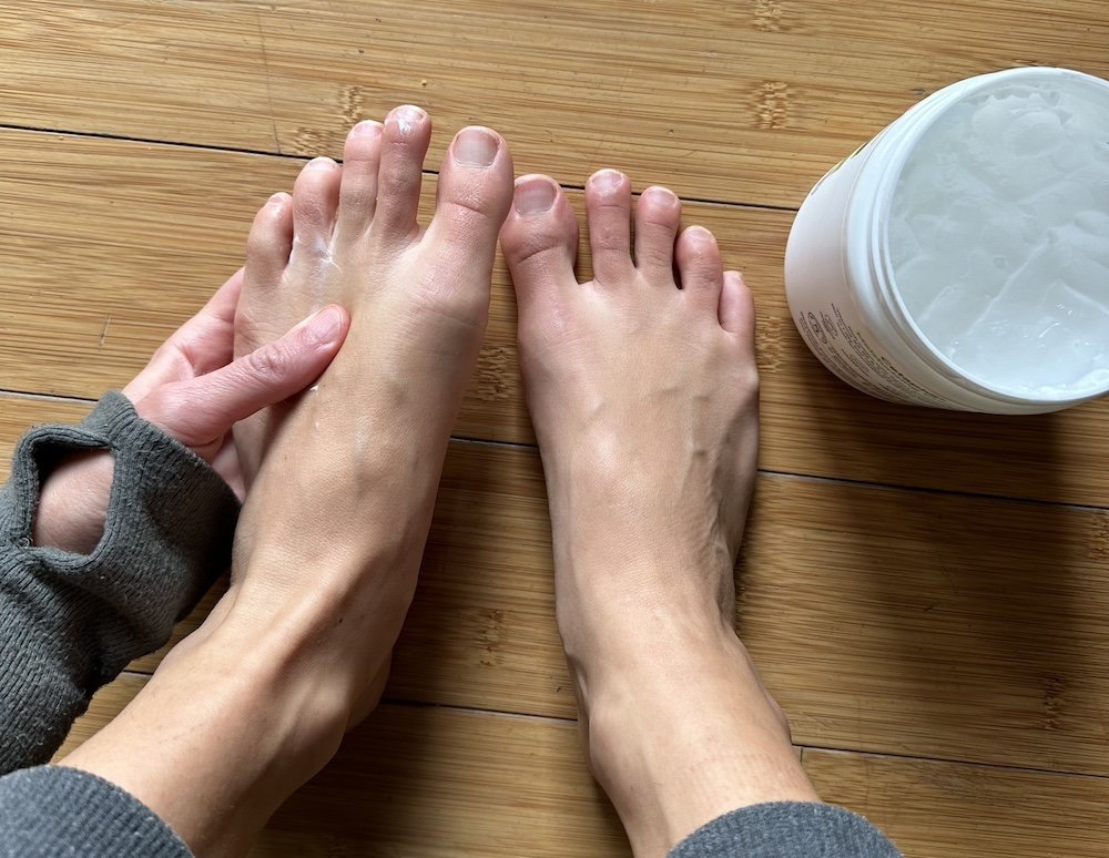 Close up of a pair of bare feet getting moisturizer rubbed in used as a header image for foot skin care for barefooters