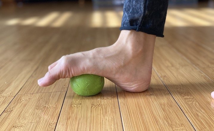 A bare foot curled over a yoga ball to show how you can massage your foot to make it more mobile to relieve bunion pain and tightness