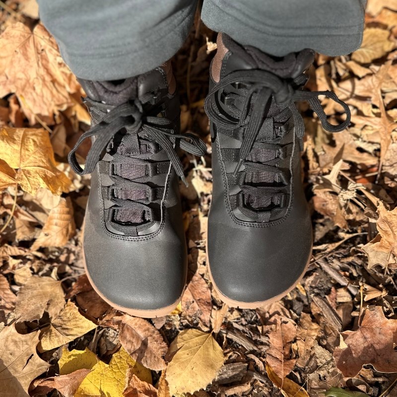 Top down close up of a pair of wide toe box lace up winter boots from Freet Barefoot. The Freet Arken 2 is shown on fallen leaves with gray wide leg sweatpants at the top of the boots.