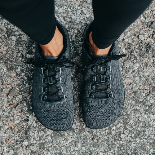 Top down view of Freet Pace mesh vegan barefoot sneakers in grey being worn by a person standing on concrete. The extra wide toe box for balance and stability is displayed