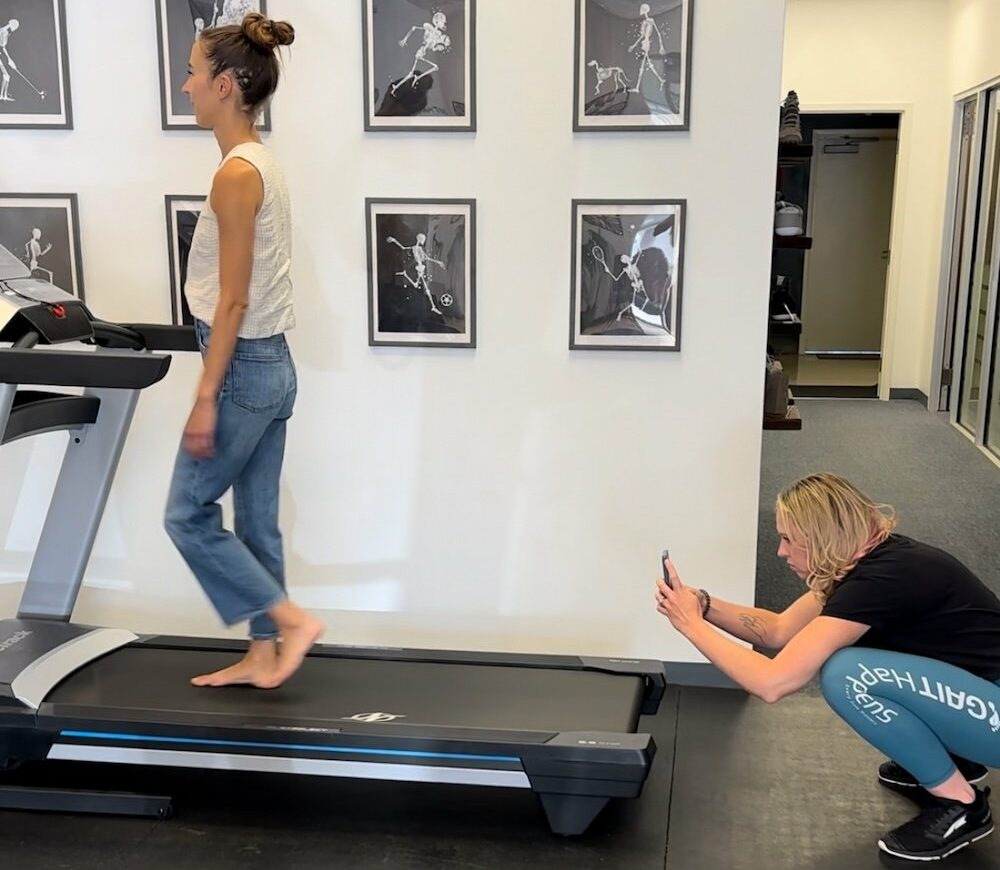 A woman walking on a treadmill with a gait specialist behind her filming to do a gait analysis