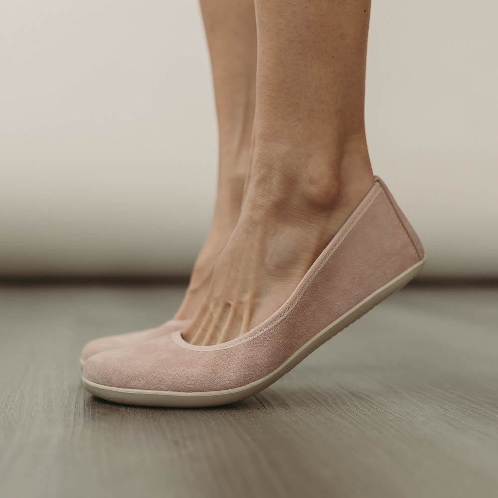 A woman wearing Groundies Lily soft pink barefoot ballet flats and standing on the balls of her feet to show their flexibility