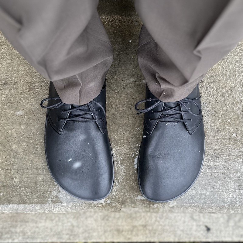 A top down view of a man wearing dress pants and black Groundies Milano desert boots in Barefoot+ wide width