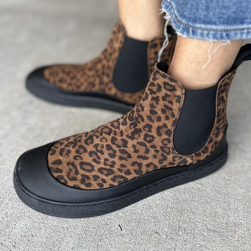Close up side view of a pair of feet standing on concrete wearing leopard print wide toe box barefoot chelsea boots - the Groundies Sienna