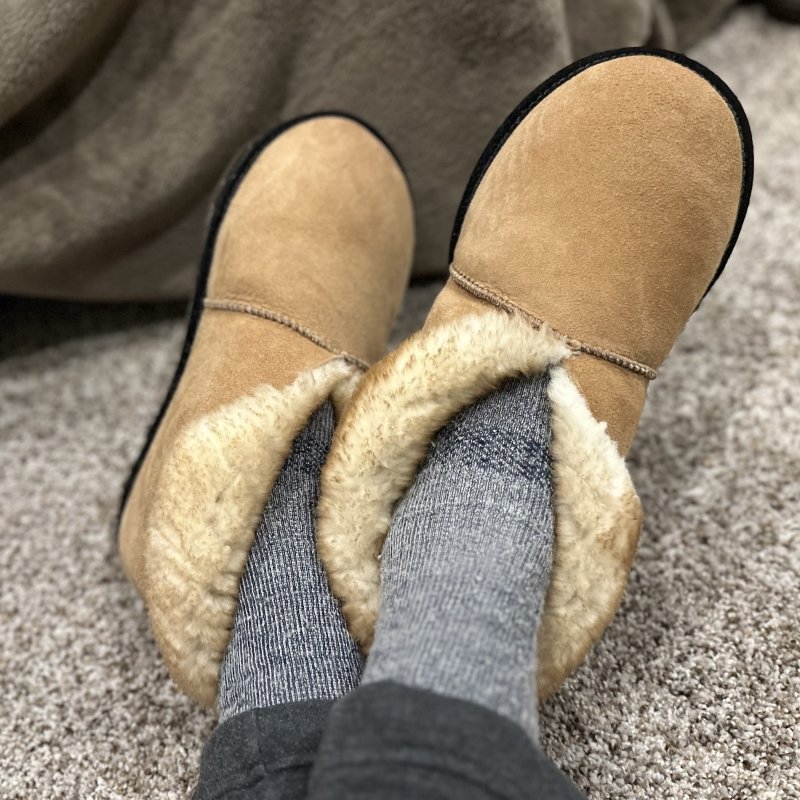 Close up view of a pair of feet crossed wearing High Plains Sheepskin slippers with a wide toe box and flat outsole