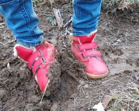 A little boy's leg wearing Ten Little Everyday High Top shoes standing in mud.