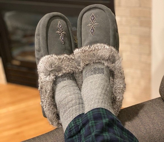 a pair of feet propped up wearing barefoot manitobah mukluk moccasin slippers
