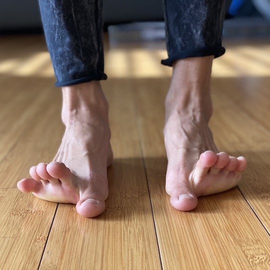 A close up of a woman's feet. Her big toes are flat on the floor and her other toes are raised up.