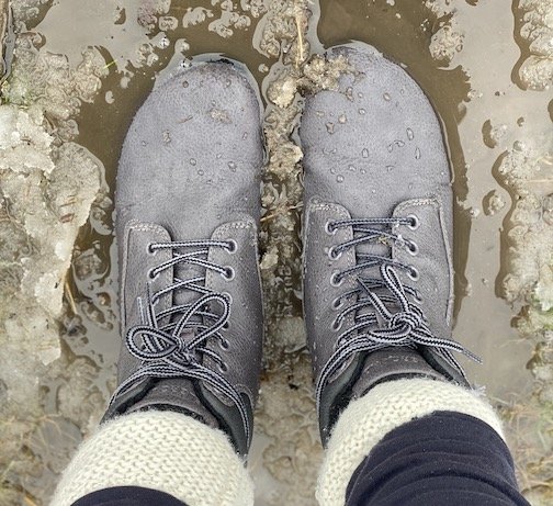 A top down close up of Feelgrounds Patrol, a vegan barefoot winter boots, standing in a puddle of yucky muddy snow.