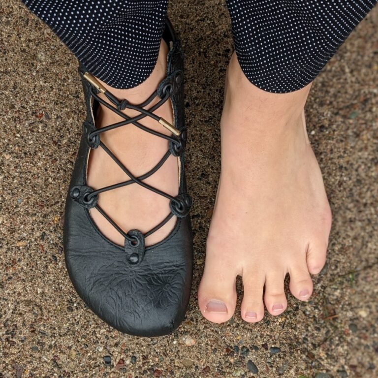Top Down view of a person's feet with one bare and one wearing Jenon Leather J Joplin pumps wide stylish barefoot flats