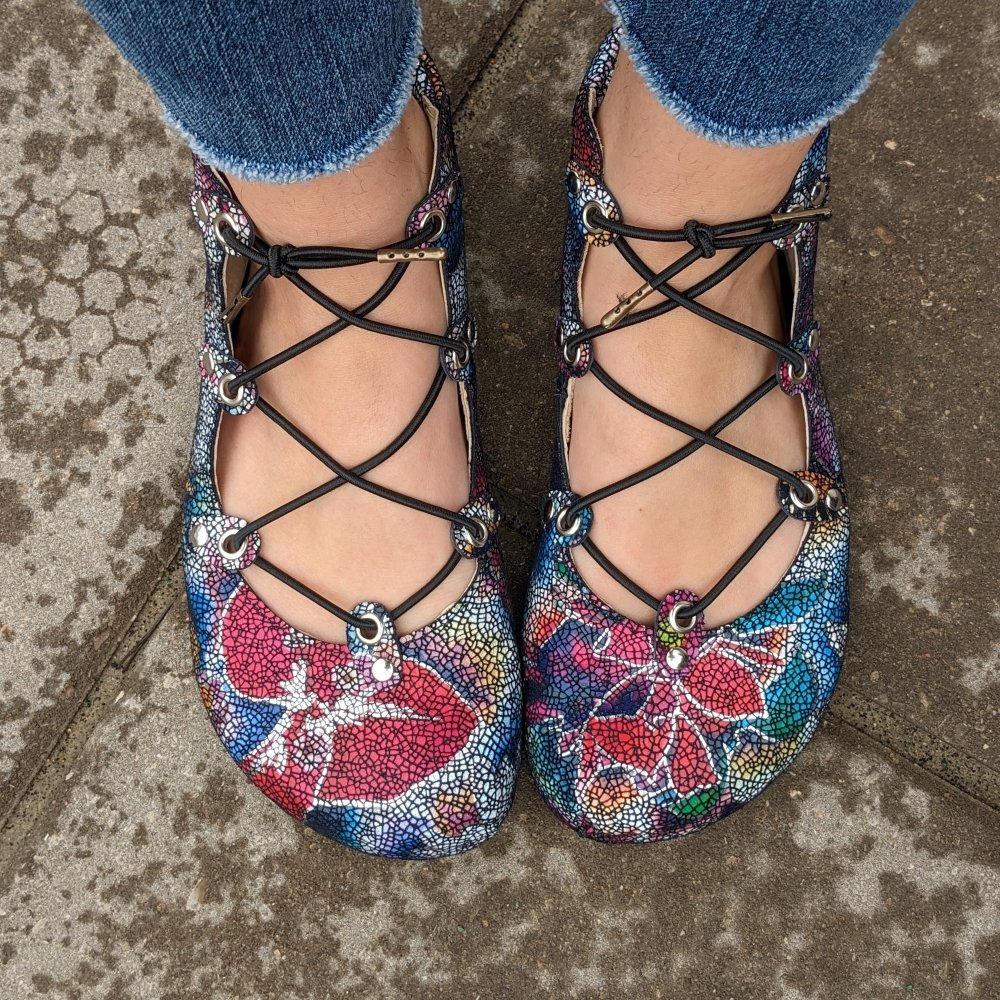 Top down view of a woman's feet in unique lace up ballet flats in a metallic floral print and black elastic laces. The toe box is an extra wide anatomical shape