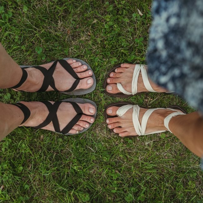 Top down view of two people both wearing Juuri multi tie barefoot sandals in black and white fabrics.