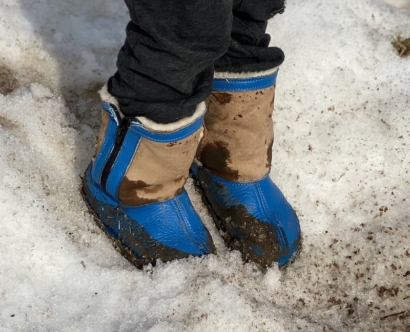 A child standing in dirty snow wearing wide toe box barefoot winter boots from Softstar - the Phoenix sheepskin wool leather boot