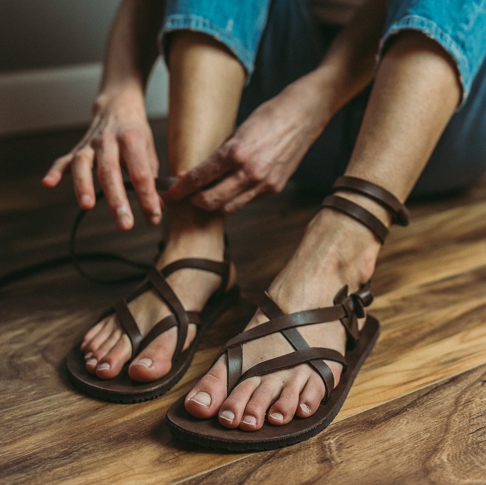 A side view of a person putting on a pair of brown Laboo leather barefoot sandals