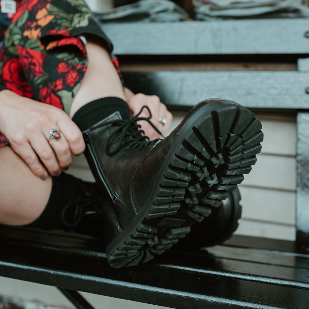 A close up view of a foot resting on a bunch with the tread of the Lang.s S black barefoot Kombat boot outsole visible