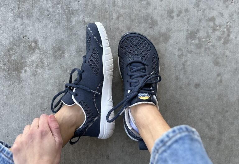 A pair of feet resting on concrete wearing blue Lems Shoes Primal 3 barefoot sneakers