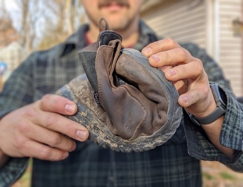 A man holding a Lems Chelsea waterproof barefoot zero drop minimalist boot in Espresso folded up to show its flexibility