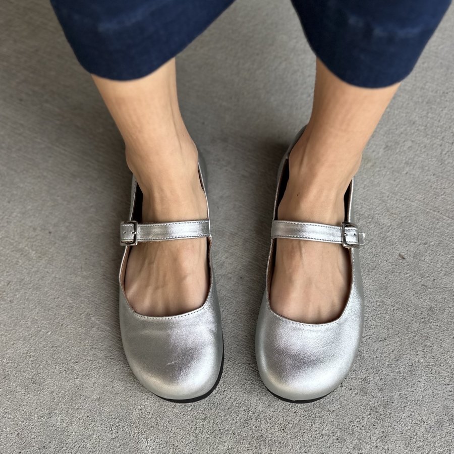 Top down view of Lisbeth Joe Paris Silver Mary Janes with a wide toe box and functional buckle strap. There is dark denim cropped pants just visible at the top of the frame.