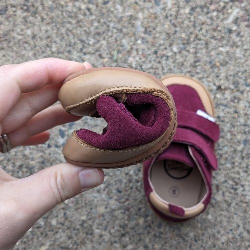 A close up of a hand squishing a Little Love Bug barefoot kids shoe into a C shape to show flexibility