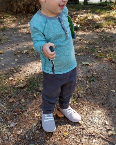 A young boy in jogger pants and a henley holding car keys and wearing Little Love Bug barefoot oxford shoes with elastic laces