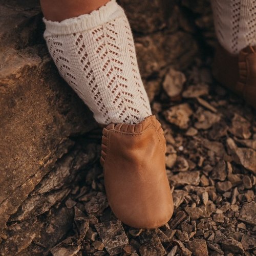 Close up of a chubby toddler leg wearing textured knee high socks and ankle ruffle leather booties from Little Love Bug with a wide toe box