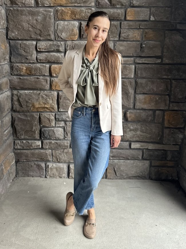 Full body photo of a woman with long brown hair wearing a pair of jeans, a silky green blouse, and a cream colored blazer. She has Be Lenka Viva Loafers on her feet