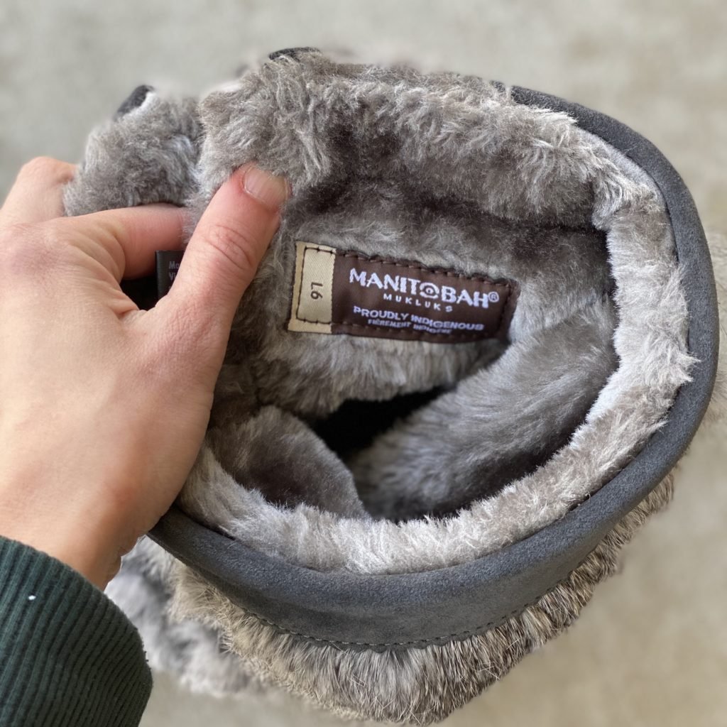 A woman's hand holding the top of Manitobah Mukluks winter boots showing the faux faur lining.