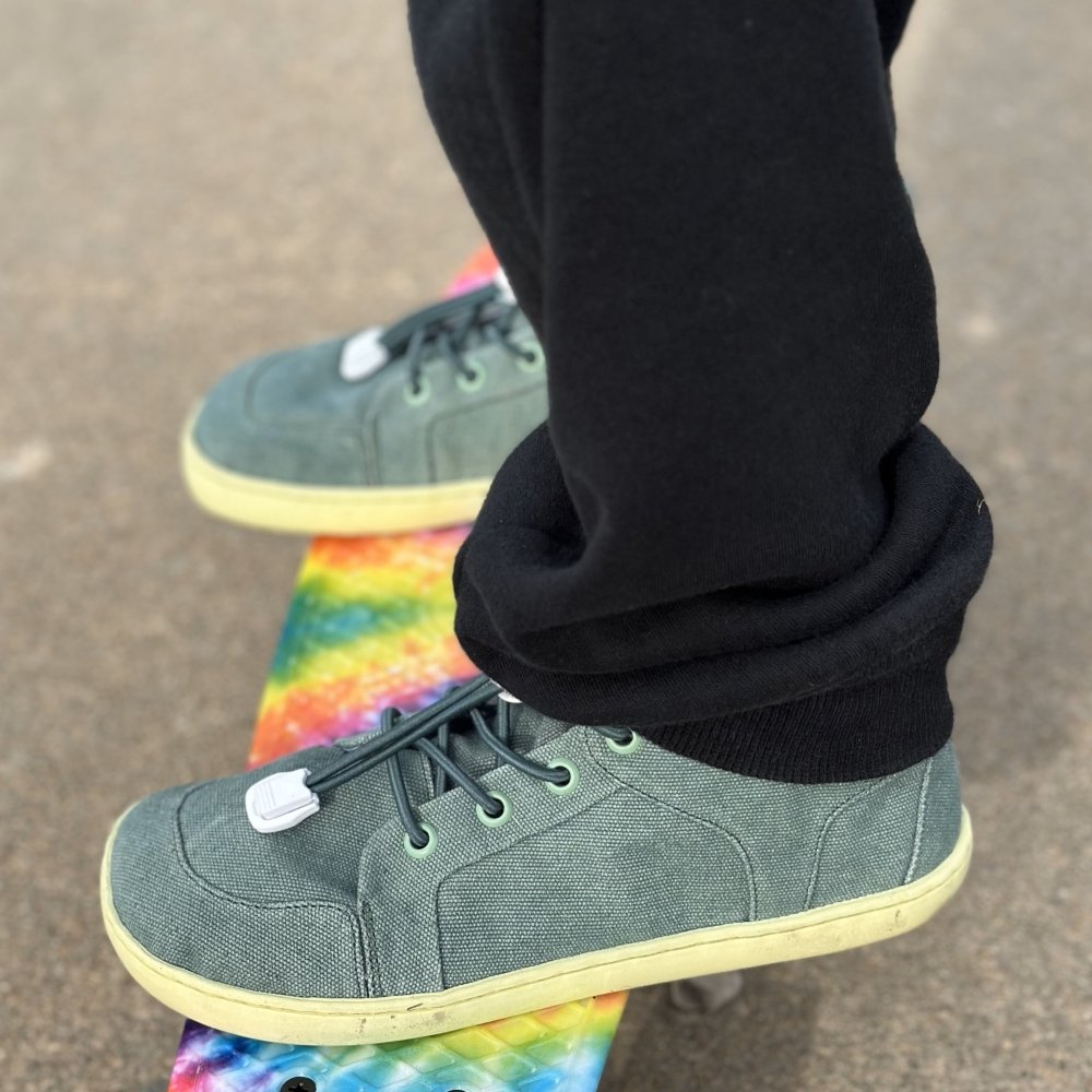 Close up of Kids Mukishoes Challenge blue green flexible sneaker standing on a rainbow skateboard